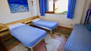 Una habitación con dos camas individuales, una mesita pequeña, una lámpara, un cuadro, una ventana con cortinas y un suelo de baldosas.