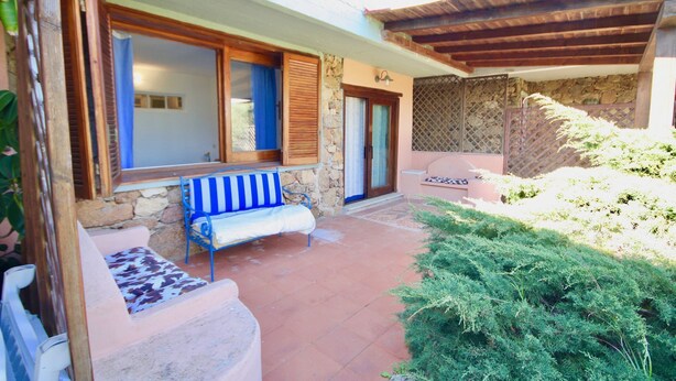 Un espacio al aire libre cubierto con un banco de piedra, una pérgola de madera y un pequeño jardín.