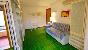 Une pièce avec un sol carrelé de carreaux verts, un canapé à rayures, une petite table avec une chaise et une lampe.