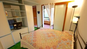 Une chambre à coucher avec un lit, une armoire, un bureau avec un ordinateur et une fenêtre avec des rideaux.
