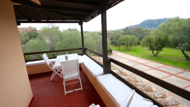 Un espace extérieur aménagé, abrité et doté de tables et de chaises, offrant une vue sur un jardin paysager avec des arbres et une montagne au loin.