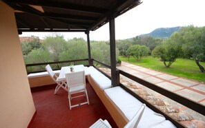 A covered outdoor seating area with a table and chairs, overlooking a landscaped garden with trees and a distant mountain. - Casa Carla (Olbia)