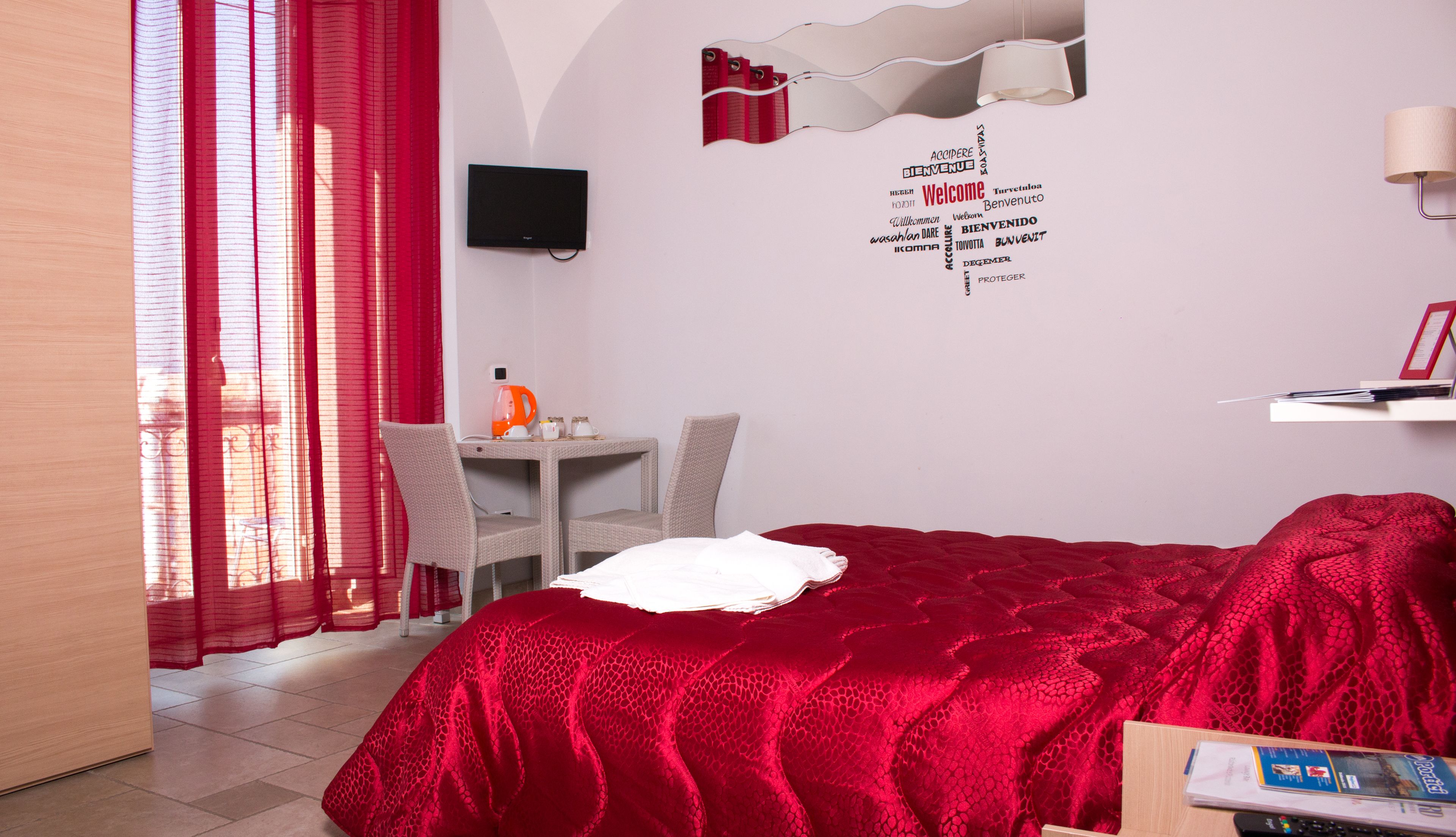 A hotel room with a bed, a desk with a chair, a television, and a red curtain.