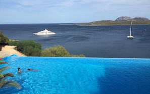 A pool with clear blue water, a yacht in the background, and a sailboat on the water. - Casa Marinella (Olbia)