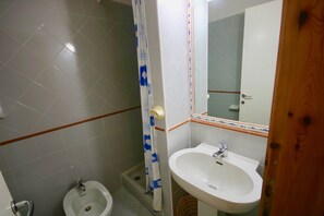 A bathroom with a white sink, a bidet, and a shower with a blue curtain.