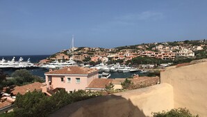 Une ville côtière dotée d’un port de plaisance, de bâtiments aux toits de tuiles rouges et d’une colline où se trouvent des habitations.
