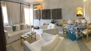 Un salon bien éclairé, comprenant un canapé, des fauteuils, une table basse et un coin repas avec une table mise pour deux personnes.