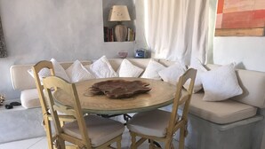 Une table ronde en bois, surmontée d’un set de table en cuir, est entourée de quatre chaises dotées d’assises rembourrées et de structures en bois. Un canapé beige avec des coussins blancs est placé derrière la table.