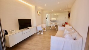 A modern living room with a flat-screen TV, white furniture, and a wooden floor.