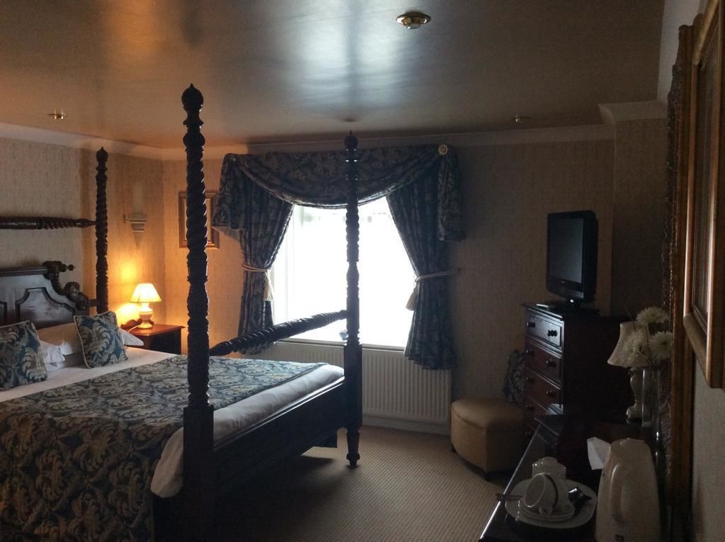 A four-poster bed with a canopy, a television on a dresser, and a small table with a vase of flowers.