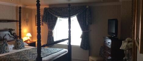 A four-poster bed with a canopy, a television on a dresser, and a small table with a vase of flowers.