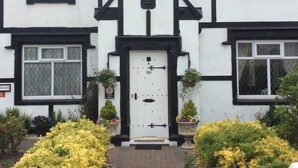 A traditional half-timbered house with a white facade and black timber framing, a central door with a number plate, and a brick pathway leading to the entrance. - The Old Coach House (Blackpool)