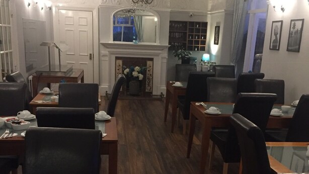 A hotel dining area with wooden flooring, black chairs, and tables set for dining. - The Old Coach House (Blackpool)
