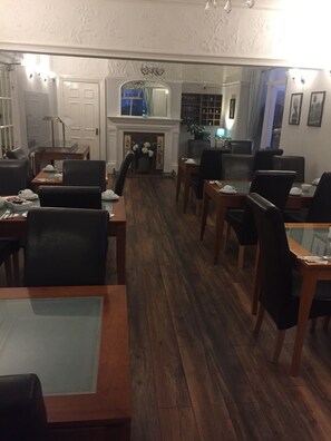 Zona de dinar d'hotel amb terres de fusta, cadires negres i taules preparades per a dinar.