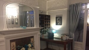 A room with a fireplace, a mirror, a table with glassware, and a window with curtains. - The Old Coach House (Blackpool)