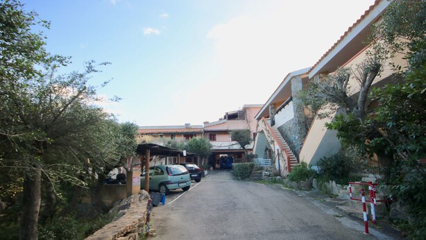 A narrow street with parked cars and a building with a stone facade. - Casa Rosa (Olbia)