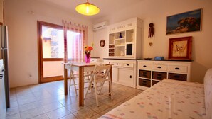 A cozy kitchen with a dining area, a refrigerator, a window with curtains, and a painting on the wall. - Casa Rosa (Olbia)