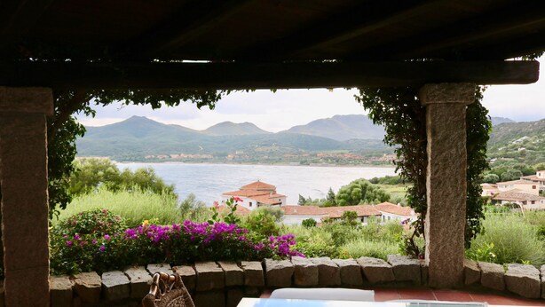 A view from a covered outdoor area with a stone wall, a table, and a chair. - Casa Turchese (Olbia)