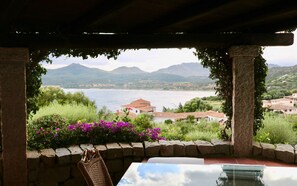 A view from a covered outdoor area with a stone wall, a table, and a chair. - Casa Turchese (Olbia)
