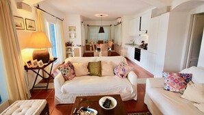 A living room with a sofa, a coffee table, and a dining area with a table and chairs. - Casa Turchese (Olbia)