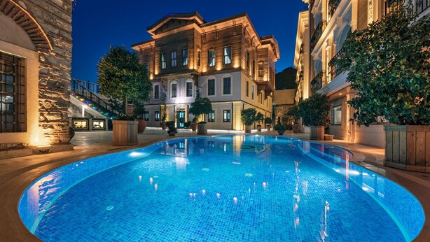 A large, well-lit swimming pool surrounded by stone buildings with balconies and potted plants. - Seven Hills Palace & Spa (Istanbul)