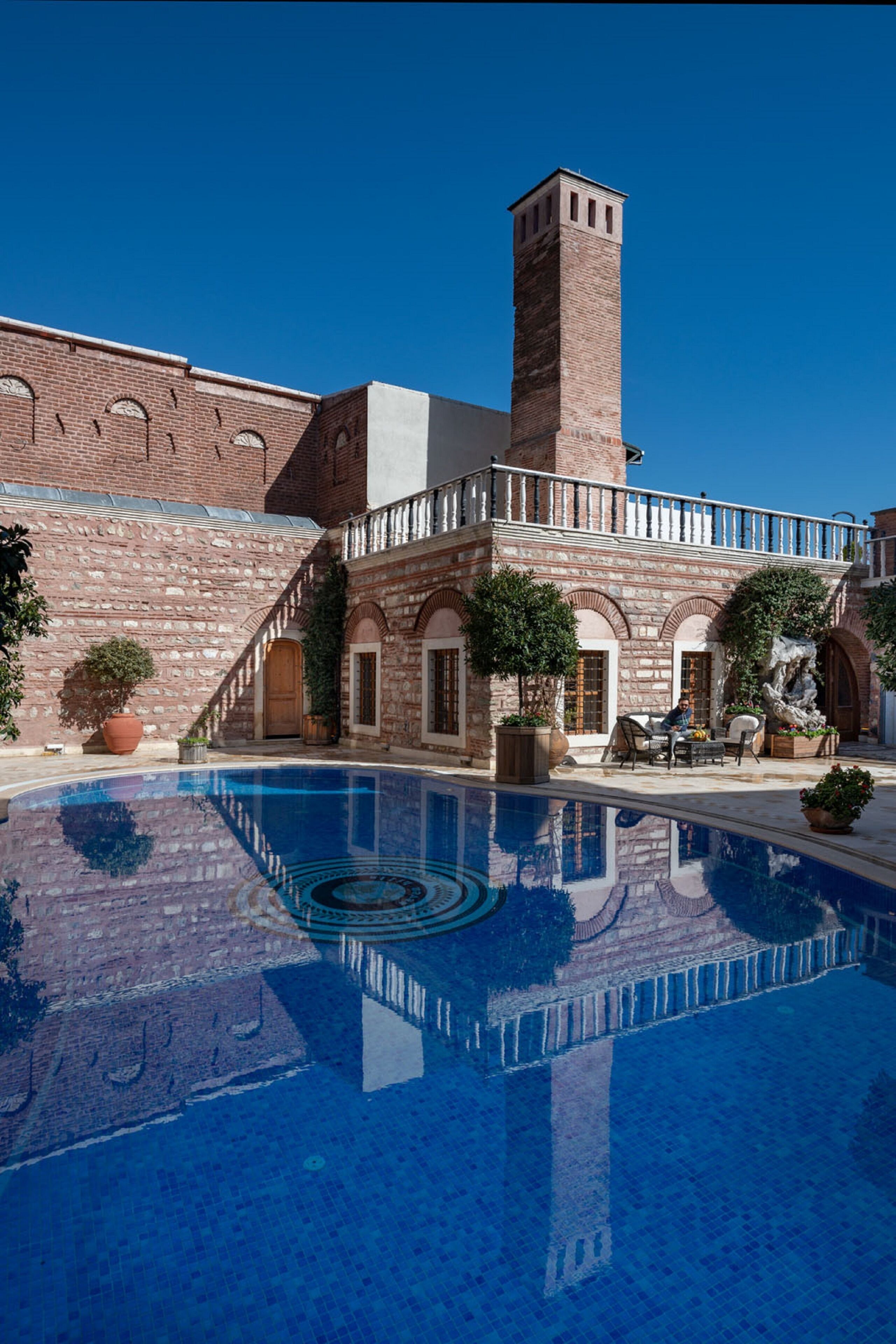 A courtyard with a swimming pool, a brick building with arched windows, and a tall chimney.