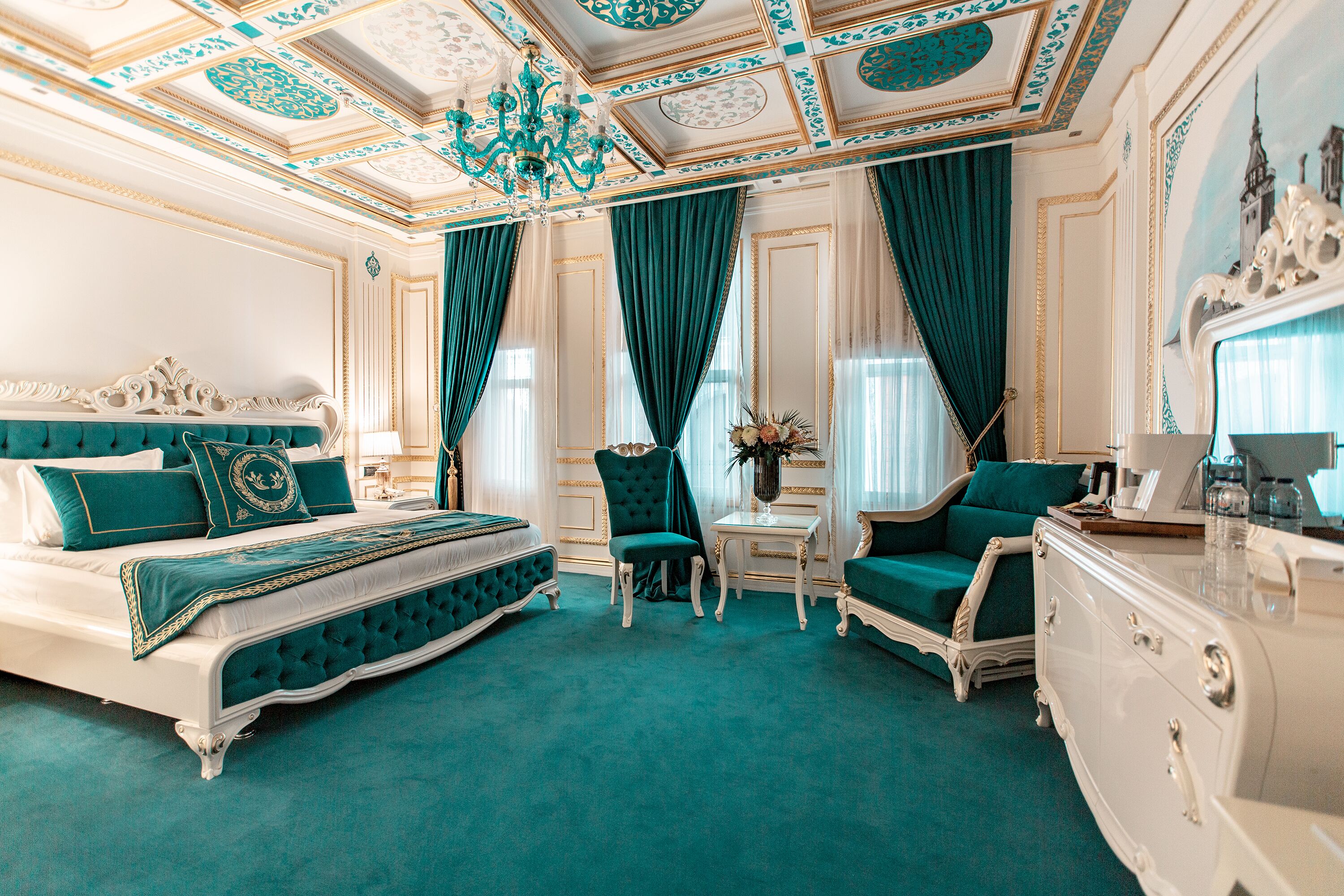 A luxurious bedroom with a large bed, a chaise lounge, a dresser, and a small table with a vase of flowers.