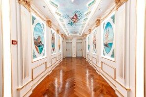 Un pasillo con detalles dorados ornamentales, piso de madera pulida y grandes cuadros ovalados en las paredes.