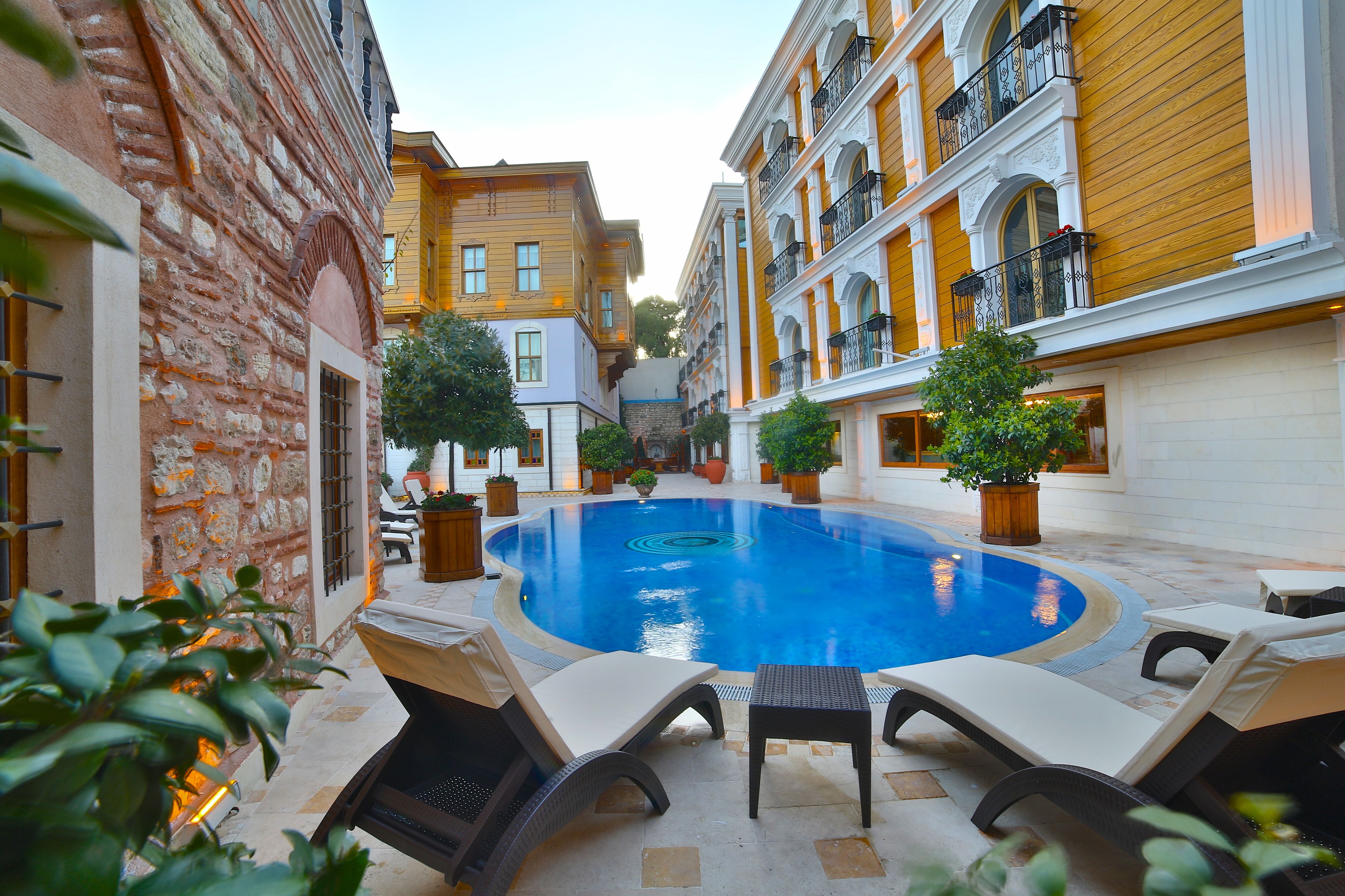 A swimming pool with lounge chairs, surrounded by buildings with balconies and potted plants.