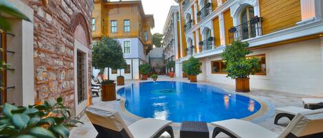A swimming pool with lounge chairs, surrounded by buildings with balconies and potted plants.