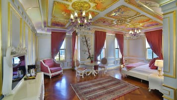 A luxurious room with a large bed, a sitting area with a table and chairs, and a chandelier.