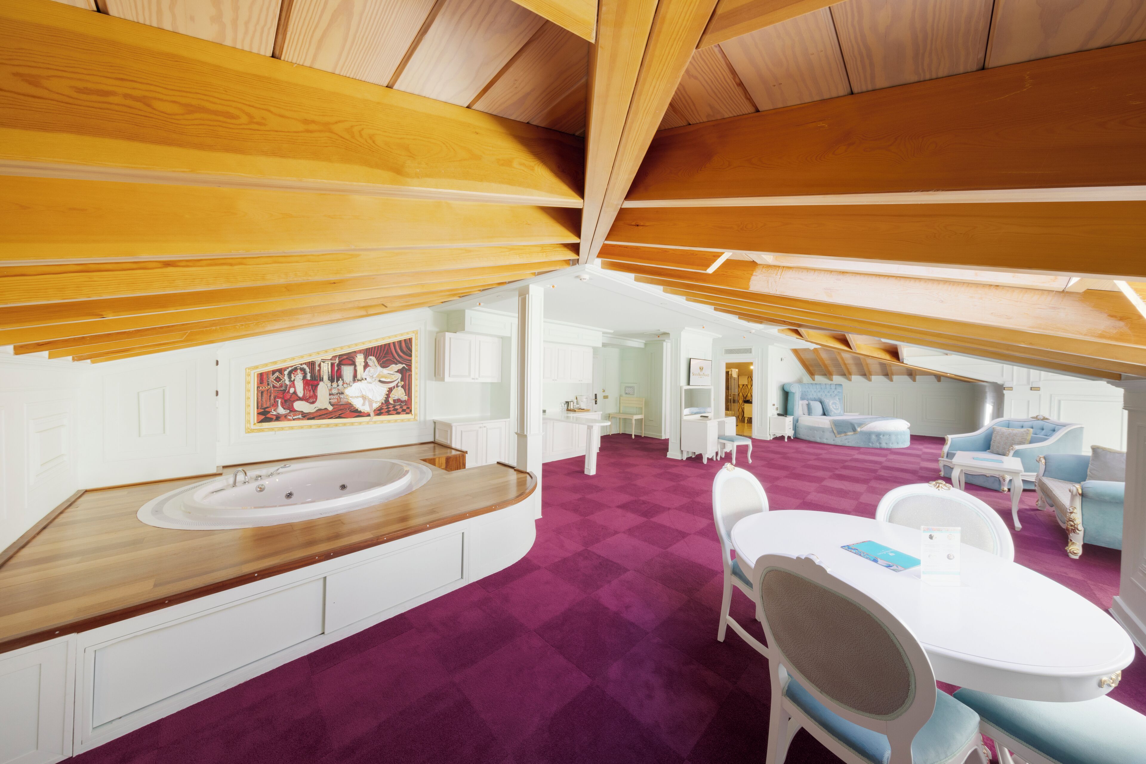 A spacious room with a large wooden ceiling, a white bathtub, a purple carpet, and a dining area with white furniture.
