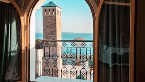 A view through an arched window of a balcony with a wrought iron railing, a stone tower, and a clear blue sky. - Seven Hills Palace & Spa (Istanbul)