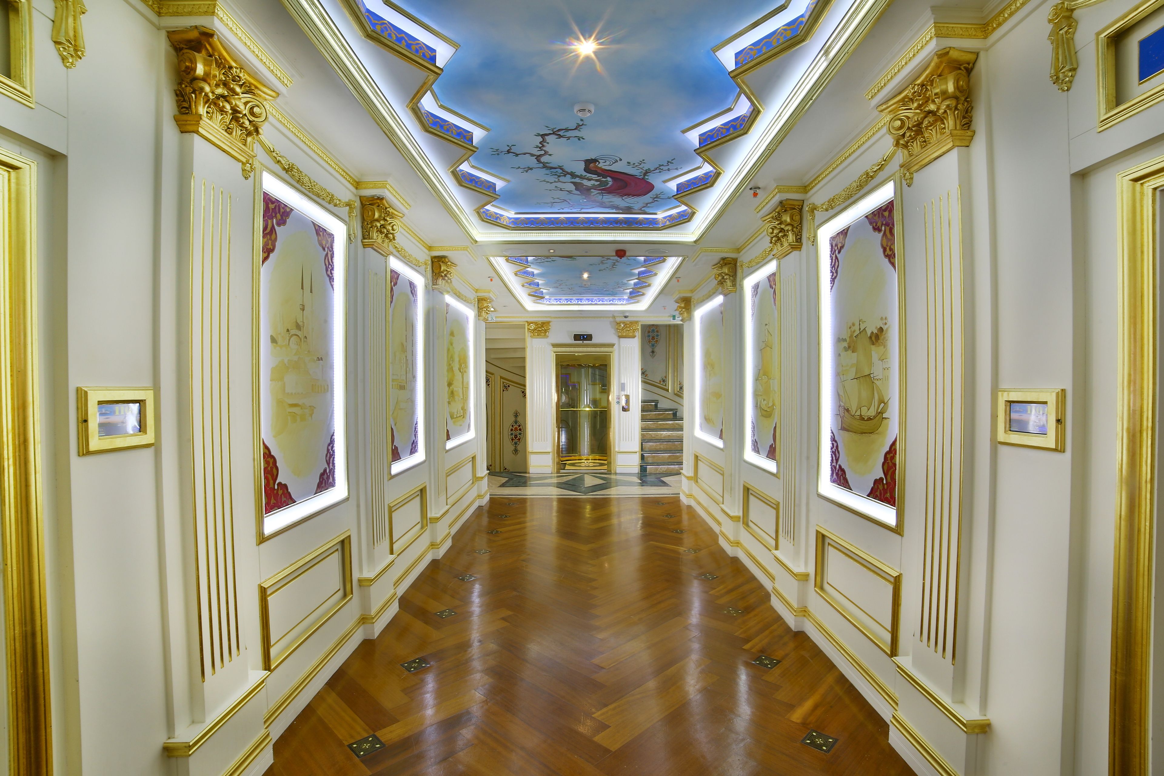 A grand hallway with ornate gold detailing, a polished wooden floor, and a ceiling with a starry design.