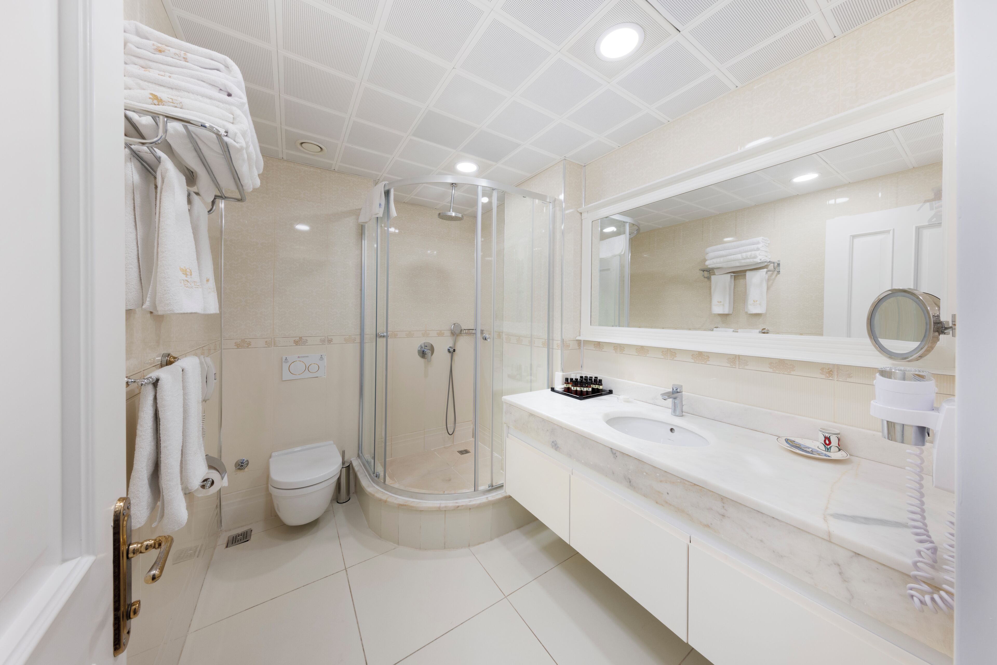 A modern bathroom with a glass-enclosed shower, a white sink with a marble countertop, and a large mirror above the sink.