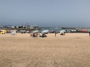 A sandy beach with umbrellas and beach chairs, a pier in the background, and the ocean. - Au Coeur Des Plages De Harhoura Rabat (Harhoura)