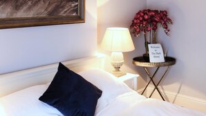 Una cama bien tendida con almohadas blancas y azul oscuro, un cuadro de paisaje enmarcado en la pared, una lámpara y una mesita con un cartel que dice "Welcome to The Dark Horse".