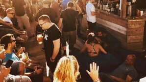 Un evento al aire libre concurrido, con gente sentada y de pie alrededor de una zona de bar.