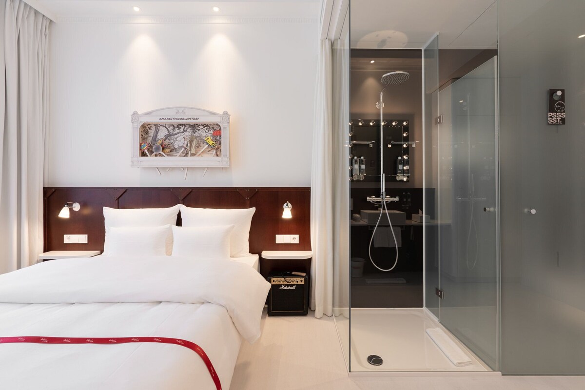 A hotel room with a large bed, bedside lamps, a shower, and a glass-enclosed walk-in closet.