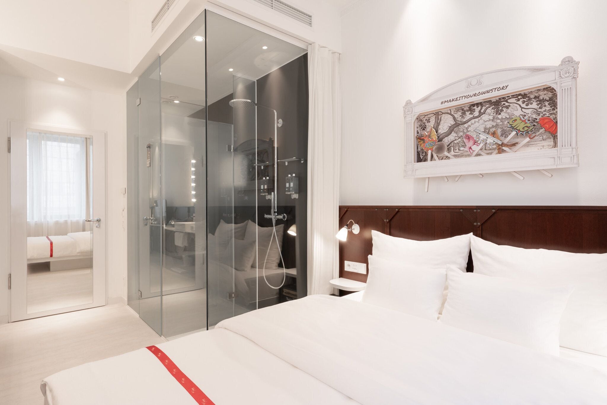 Una habitación de hotel moderna con una cama grande, un vestidor con paredes de cristal, una ducha con puerta de cristal y una obra de arte colgada en la pared.
