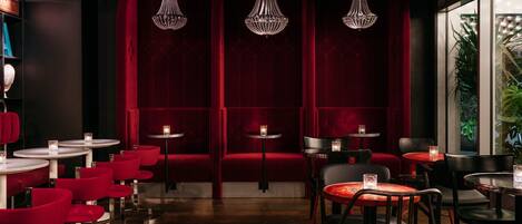 A restaurant with red velvet booths, round tables, and hanging crystal chandeliers.