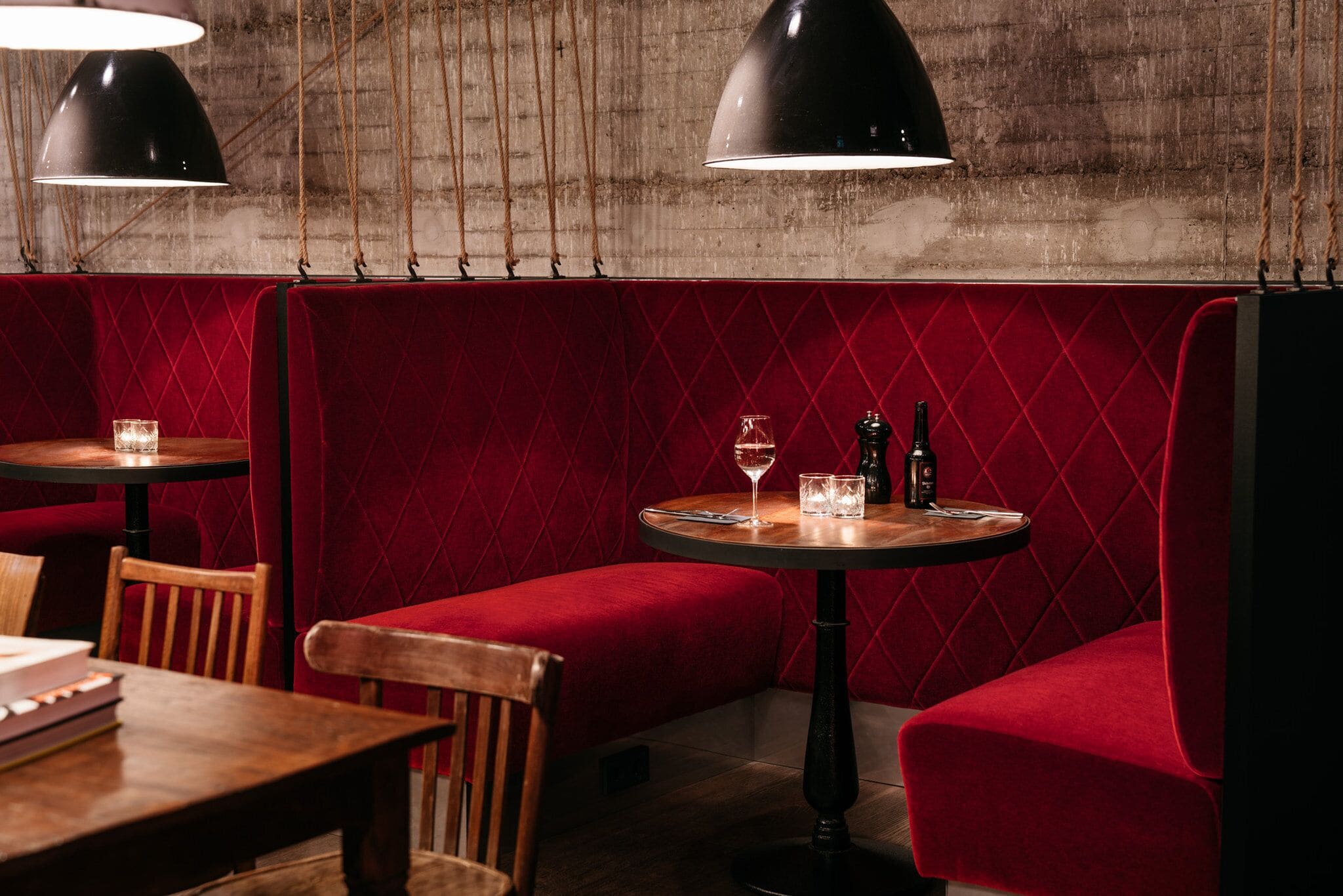 A restaurant interior with red cushioned booths, wooden tables, and hanging pendant lights.