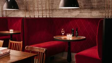 A restaurant interior with red cushioned booths, wooden tables, and hanging pendant lights.