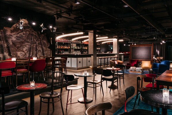 A bar area with tables and chairs, a bar counter with bottles, and a mural on the wall.