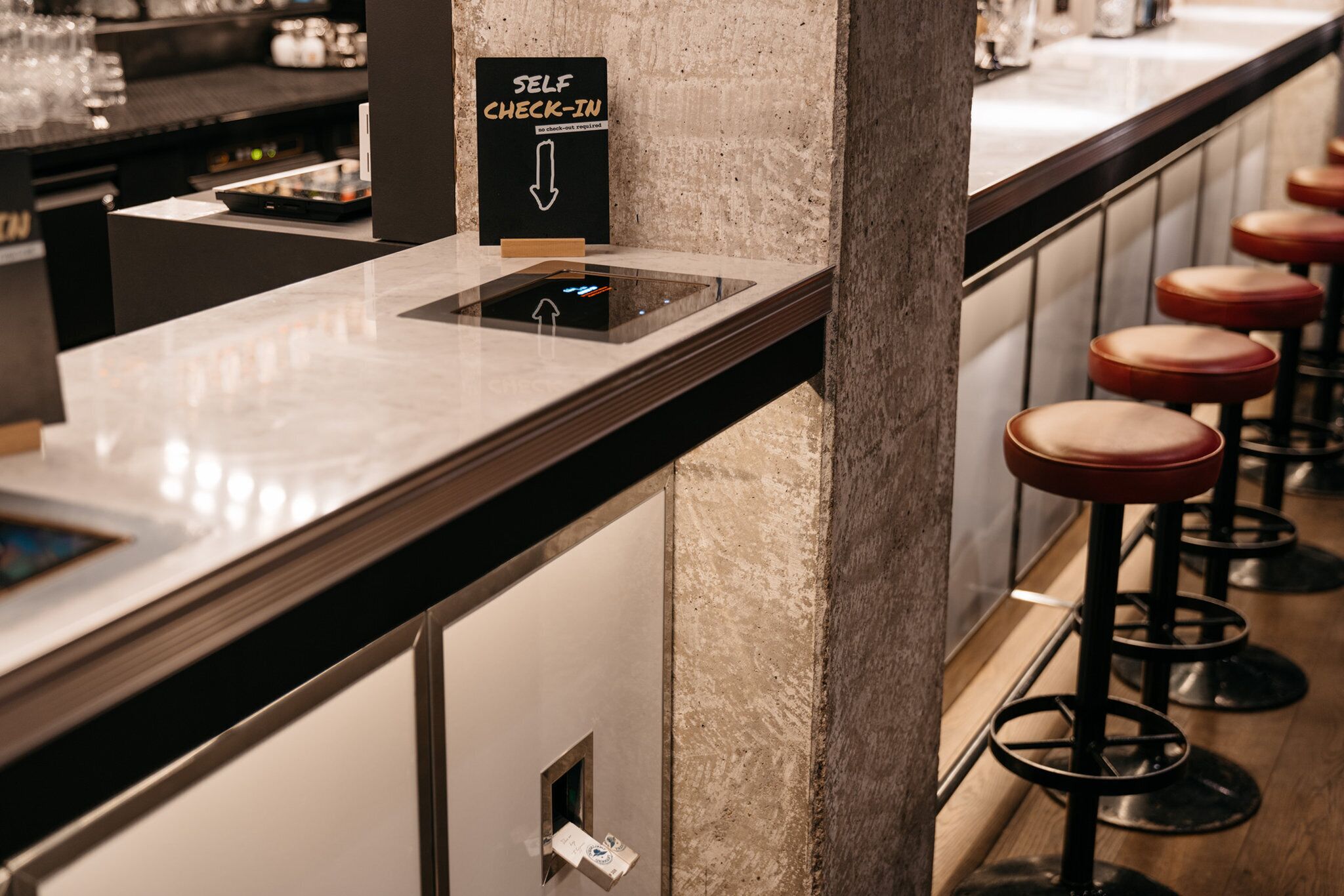 A self-check-in station with a digital kiosk, bar stools, and a marble countertop.