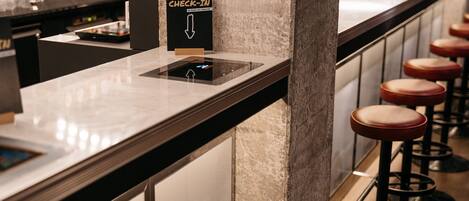 A self-check-in station with a digital kiosk, bar stools, and a marble countertop.