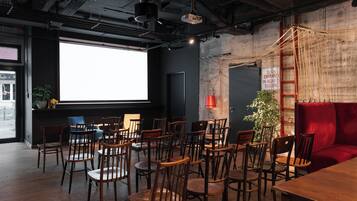 A conference room with wooden chairs and tables, a projector screen, and a red sofa.