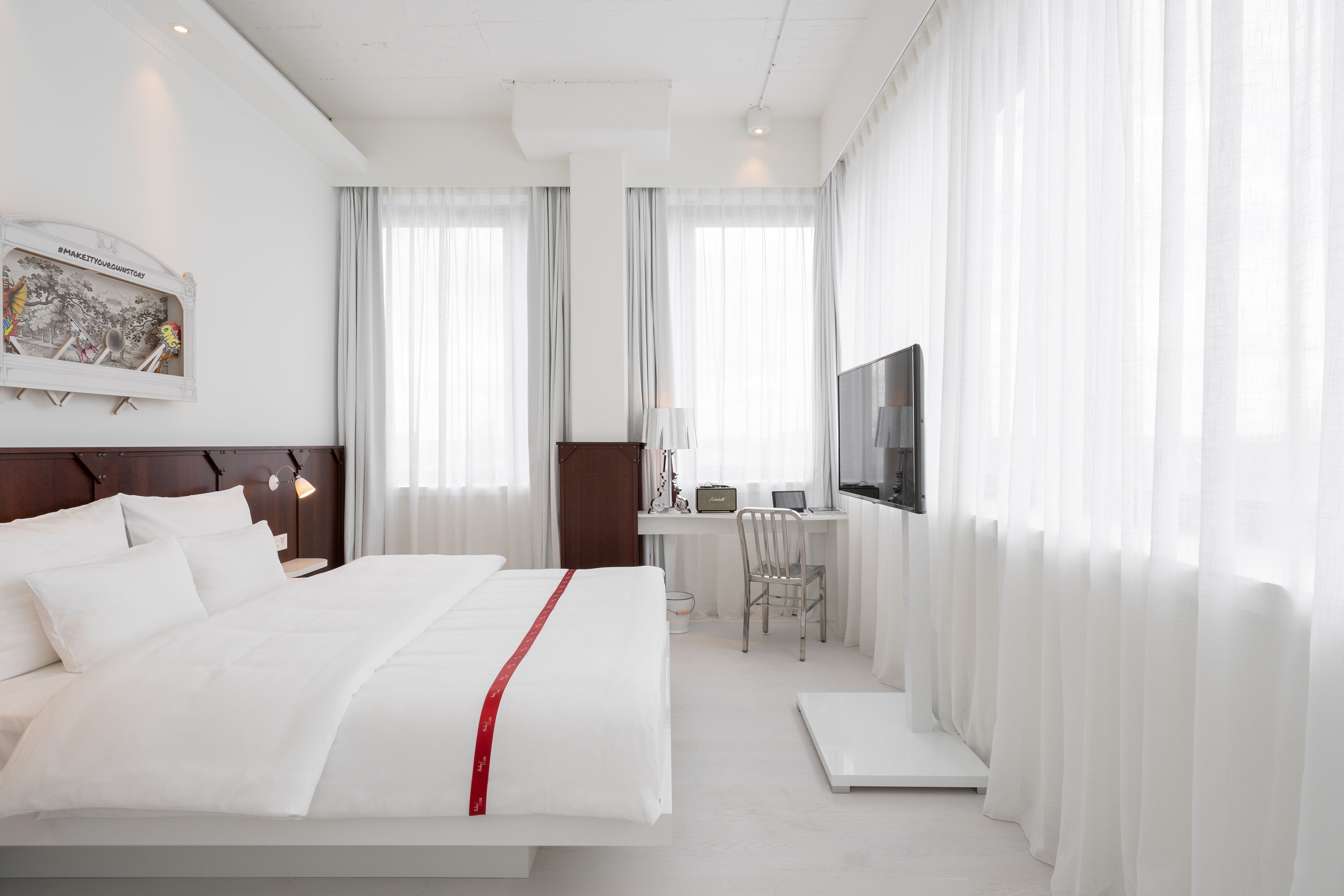 Habitación de hotel con cama, escritorio, silla, televisor y cortinas.