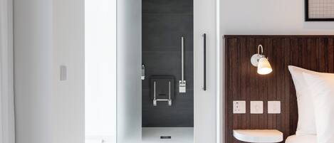 A modern bathroom with a shower, toilet, and a bedside table with a lamp.
