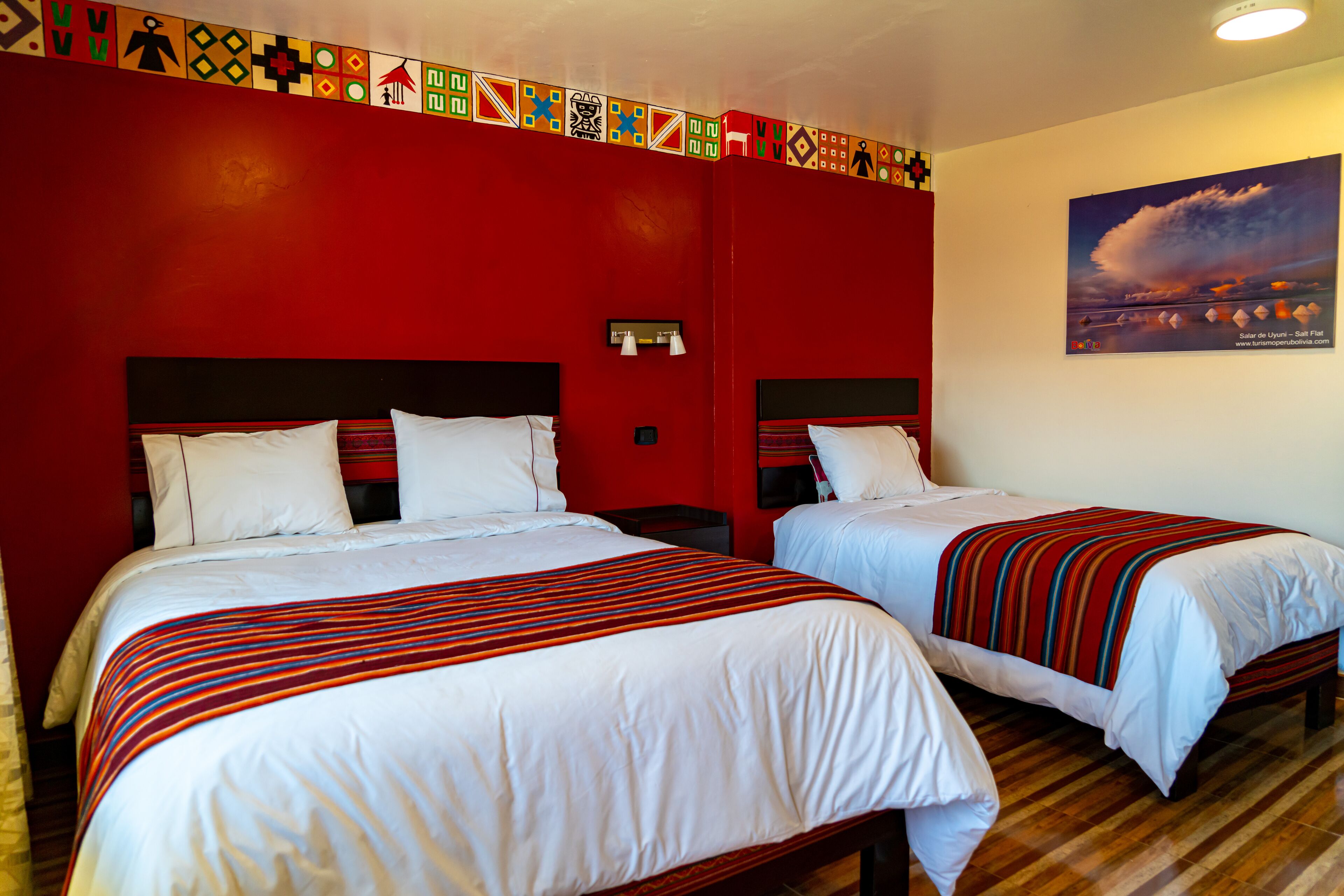 Habitación de hotel con dos camas, paredes rojas y un ventanal con vistas al cielo.